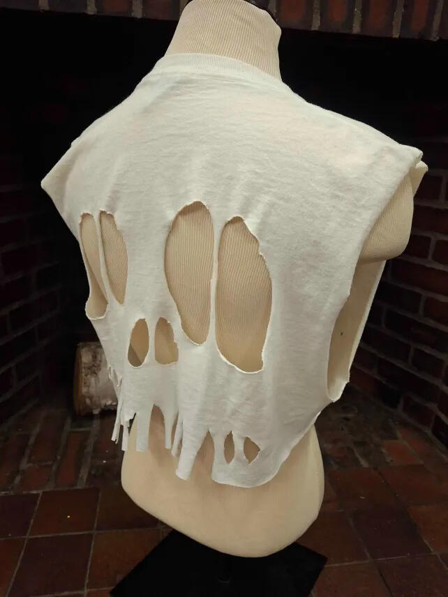 a white tee shirt cut sleeveless and cropped, with additional holes cut in the back to resemble the shape of a skull, with the holes making the mouth partially extending to the bottom of the shirt making a fray.