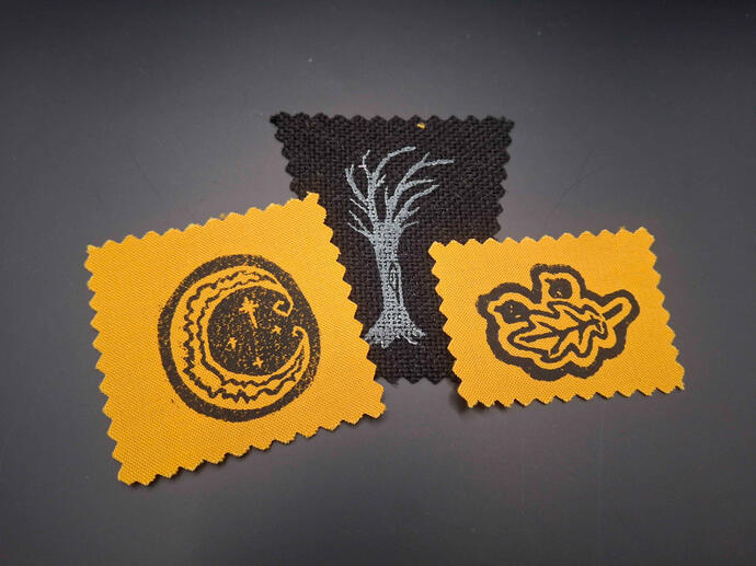Tiny block printed patches of a stylized crescent moon, a tree, and a leaf with two acorns.