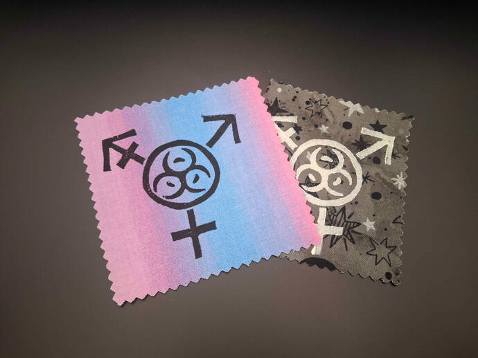 Block printed patches of the transgender symbol with the toxic radioactive symbol in the center.