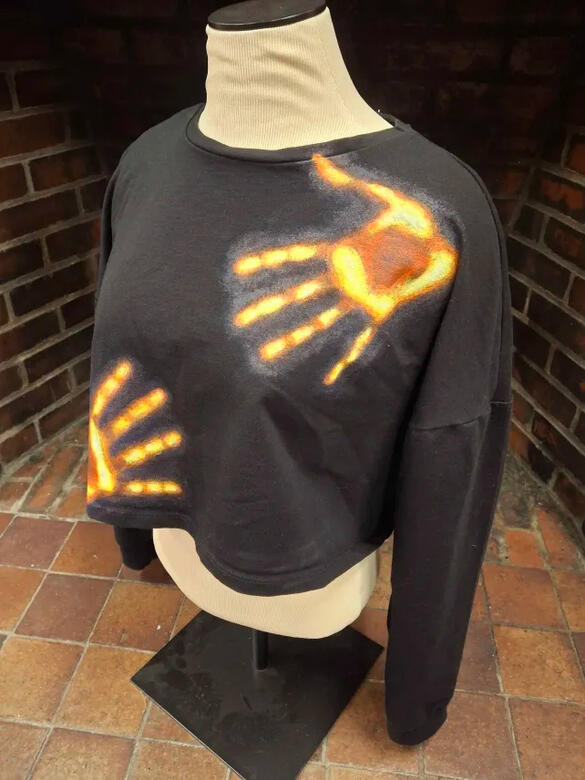 a black longsleeve cropped shirt with two hands painted on in white, yellow, red, and blue in the style of a thermal camera