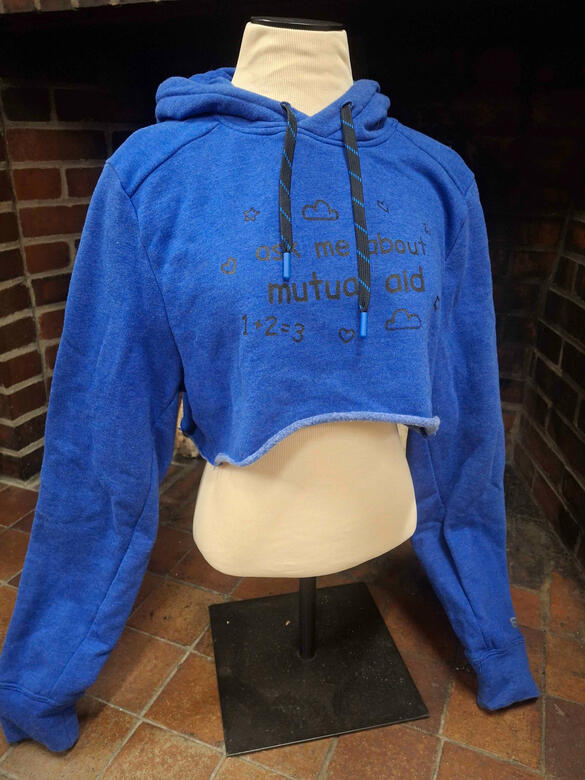 A cropped blue sporty hoodie with black and blue strings, with a screen print in black that says "asks me about mutual aid" and has simple doodles around it.