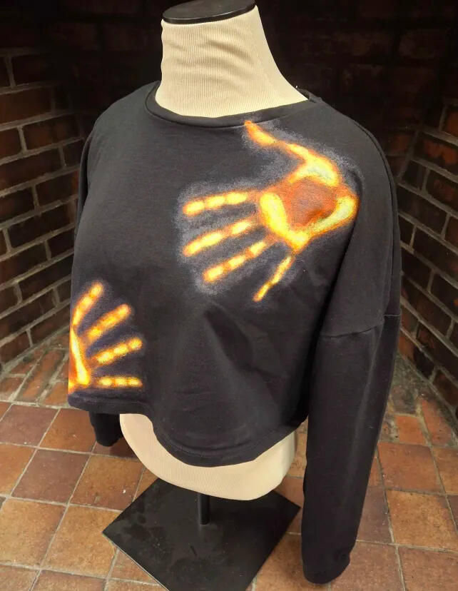 a black longsleeve cropped shirt with two hands painted on in white, yellow, red, and blue in the style of a thermal camera
